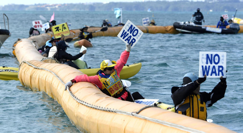 Protesters on canoes display placard as construction workers dumped a truckload of sediment on the ground and bulldozed it into the sea at Henoko on Okinawa’s east coast to build a runway for a Marine Corps base, Friday, Dec. 14, 2018. Japan's central government started main reclamation work Friday at a disputed U.S. military base relocation site on the southern island of Okinawa despite fierce local opposition. (Koji Harada/Kyodo News via AP)