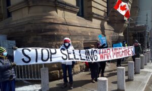 People wearing masks in the winter hold a banner that says STOP SELLING WAR MACHINES in front of the PMO office in Ottawa.