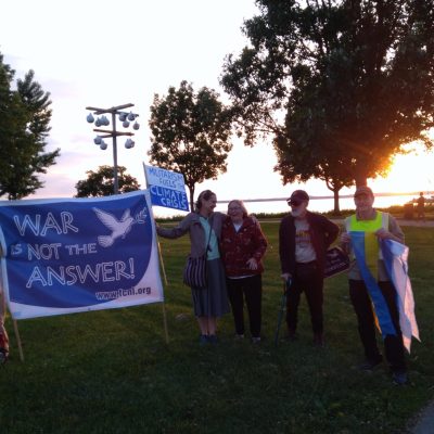 Members of the Madison chapter gather outside at sunset holding a big banner reading "War is not the answer"